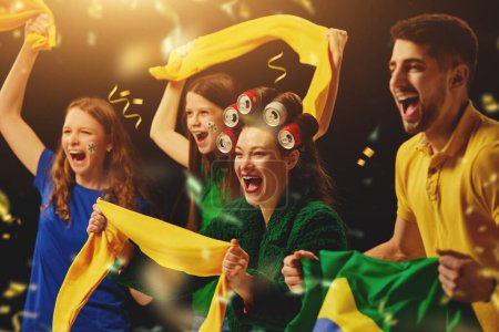 Photo for Group of young people, sport fans emotionally shouting, cheering up football team on competition over dark background with confetti. Concept of sport, leisure time, emotions, hobby and entertainment - Royalty Free Image