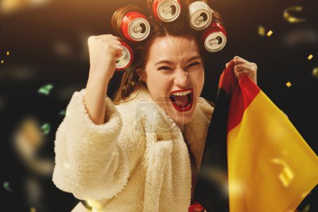 Foto de Éxito, ganar. Feliz mujer emocional, ventilador animando equipo de fútbol alemán favorito sobre fondo oscuro con confeti. Concepto de deporte, tiempo libre, emociones, hobby y entretenimiento - Imagen libre de derechos