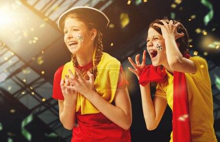 Photo for Tense game moment. Young girls emotionally watching football match, cheering team over dark background with confetti. Concept of sport, leisure time, emotions, hobby and entertainment - Royalty Free Image