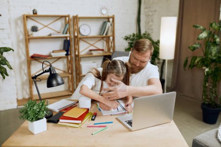 Photo for Mature man, father sitting at table and working on laptop remotely at home with little girl drawing, playing with him. Concept of fatherhood, childhood, family, freelance job, home office - Royalty Free Image