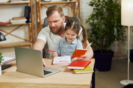 Photo for Mature man, father sitting at table and working on laptop remotely at home with his little preschool daughter drawing with him. Concept of fatherhood, childhood, family, freelance job, home office - Royalty Free Image