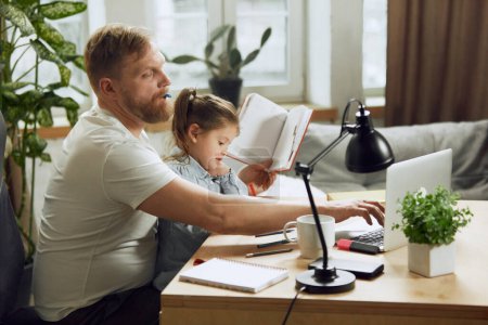 Photo for Mature man, father sitting at table and working on laptop remotely at home and playing with his little daughter. Concept of fatherhood, childhood, family, freelance job, home office - Royalty Free Image