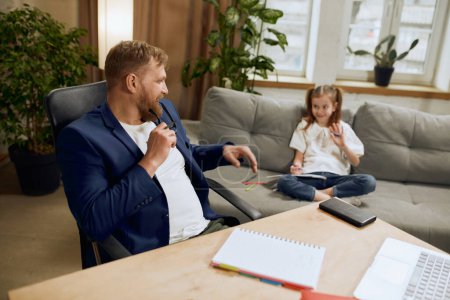 Photo for Mature man, father sitting at table and working on laptop remotely at home and talking with his little daughter. Attentive parent. Concept of fatherhood, childhood, family, freelance job, home office - Royalty Free Image