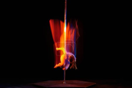Photo for Young athletic girl dancing on pylon, performing pole dance isolated over black studio background with mixed neon lights. Concept of sport and dance, beauty of movements, action, modern style - Royalty Free Image