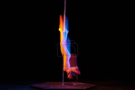 Photo for Upside down. Line. Young girl performing pole dance isolated over black studio background with mixed neon lights. Concept of sport and dance, beauty of movements, action, modern style - Royalty Free Image