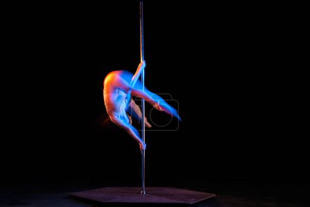 Photo for Doing tricks. Young girl performing pole dance isolated over black studio background with mixed neon lights. Concept of sport and dance, beauty of movements, action, modern style - Royalty Free Image