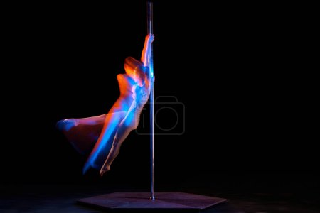 Photo for Passionate hobby. Young artistic girl performing pole dance isolated over black studio background with mixed neon lights. Concept of sport and dance, beauty of movements, action, modern style - Royalty Free Image