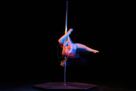Photo for Passionate hobby. Young artistic girl performing pole dance isolated over black studio background with mixed neon lights. Concept of sport and dance, beauty of movements, action, modern style - Royalty Free Image