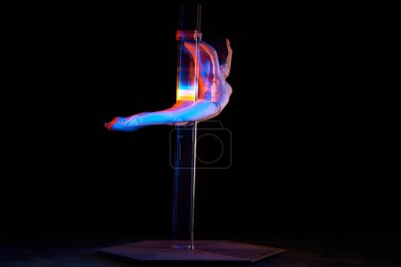 Photo for Flight of freedom. Young girl performing pole dance isolated over black studio background with mixed neon lights. Concept of sport and dance, beauty of movements, action, modern style - Royalty Free Image