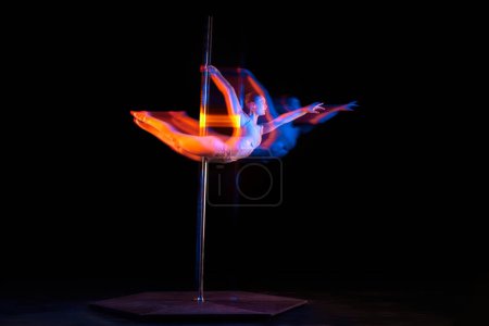 Photo for Flight of freedom. Young girl performing pole dance isolated over black studio background with mixed neon lights. Concept of sport and dance, beauty of movements, action, modern style - Royalty Free Image