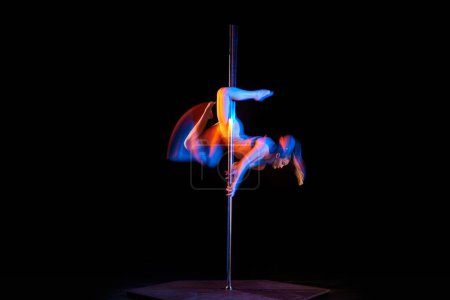Photo for Gymnastic tricks. Young girl performing pole dance isolated over black studio background with mixed neon lights. Concept of sport and dance, beauty of movements, action, modern style - Royalty Free Image