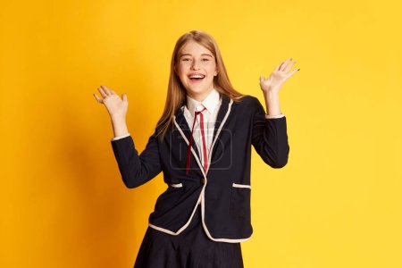 Foto de Éxito. Retrato de hermosa joven, estudiante en uniforme posando con positividad sobre fondo de estudio amarillo. Concepto de juventud, belleza, moda, estilo de vida, emociones, expresión facial. Anuncio - Imagen libre de derechos