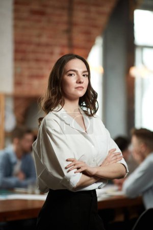 Photo for Team leader. Serious ambitious young woman in formal wear attentively looking at camera. Blurred employees on background in office. Concept of business, teamwork, career development, brainstorming - Royalty Free Image