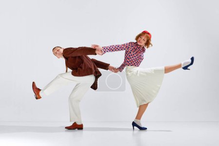 Téléchargez les photos : Jeune homme et femme en vêtements élégants dansant expressivement danse rétro sur fond de studio gris. Je m'amuse. Concept d'art, style rétro, hobby, fête, fun, mouvements, 60s, 70s culture - en image libre de droit
