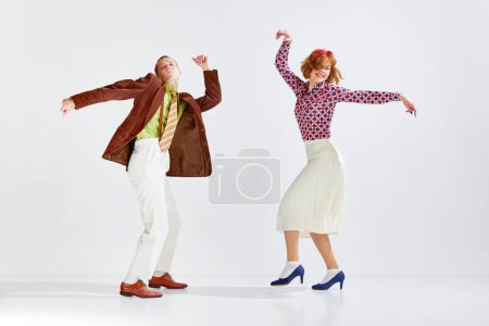 Foto de Joven hombre y mujer en ropa elegante y colorida bailando danza retro sobre fondo gris estudio. Un hobby activo. Concepto de arte, estilo retro, hobby, fiesta, diversión, movimientos, cultura de los años 60, 70 - Imagen libre de derechos