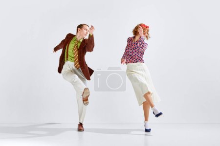 Téléchargez les photos : Jeune homme et femme dans des vêtements colorés et élégants dansant danse rétro sur fond de studio gris. Concept d'art, style rétro, hobby, fête, fun, mouvements, 60s, 70s culture - en image libre de droit