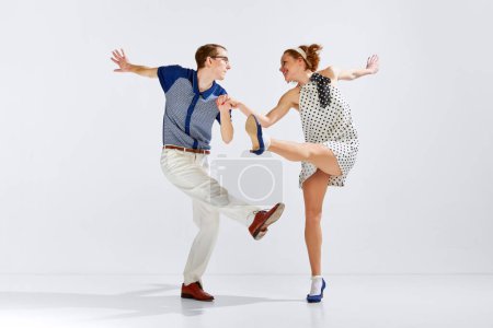 Téléchargez les photos : Des gens heureux et charmants. Jeune homme et femme en vêtements élégants dansant danse rétro sur fond de studio gris. Concept d'art, style rétro, hobby, fête, fun, mouvements, 60s, 70s culture - en image libre de droit