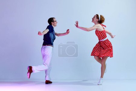 Téléchargez les photos : Styles de danse rétro. Jeune couple actif, homme et femme s'amusent. danse sur fond studio dégradé bleu violet. Concept d'art, style rétro, hobby, fête, fun, mouvements, 60s, 70s culture - en image libre de droit
