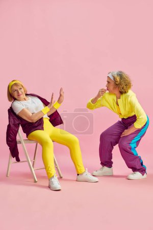 Foto de Competencia. Dos mujeres deportivas de edad avanzada en colorido entrenamiento uniforme, posando sobre fondo de estudio rosa. Concepto de estilo de vida deportivo, jubilación, atención médica, bienestar. Anuncio - Imagen libre de derechos