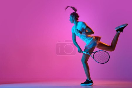 Téléchargez les photos : Balle de service avec raquette. Portrait de jeune femme, joueuse de tennis professionnelle en mouvement, s'entraînant sur fond de studio rose au néon. Concept de sport professionnel, mouvement, action - en image libre de droit