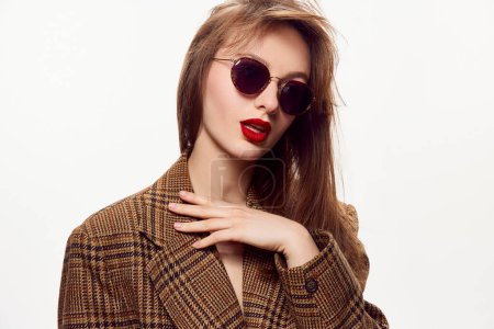 Photo for Stylish young beautiful girl with red lips, in trendy sunglasses and brown jacket posing against white studio background. Concept of skin care, cosmetology, cosmetics, natural beauty, fashion - Royalty Free Image