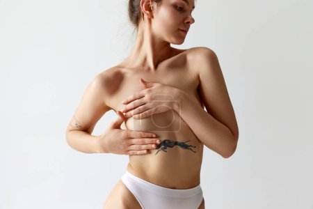 Photo for Cropped image of slim young girl covering breast with hand, posing in underwear against grey studio background. Female health care. Concept of body and skin care, figure, plastic surgery, wellness. - Royalty Free Image