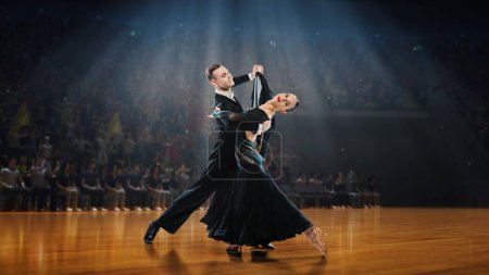 Téléchargez les photos : Beau jeune homme et femme en costumes de scène noirs attrayants performant, danse tango sur scène sous les projecteurs. Modèle 3D du public. Concept d'art, mouvements, beauté, passe-temps, style de vie - en image libre de droit