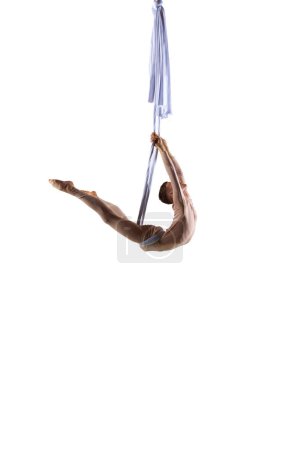 Foto de Flexible, atlético entrenamiento de gimnasta aérea masculina con cintas de seda aérea sobre fondo de estudio blanco. Cuerpo fuerte. Concepto de arte, estilo de vida deportivo, hobby, acción y movimiento, belleza - Imagen libre de derechos