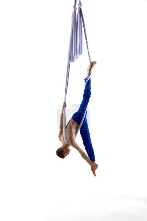 Foto de Acróbata masculino profesional, entrenamiento de gimnasta aérea con cintas aéreas, haciendo trucos contra el fondo blanco del estudio. Concepto de arte, estilo de vida deportivo, hobby, acción y movimiento, belleza, gimnasia - Imagen libre de derechos