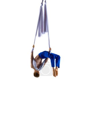 Foto de Imagen dinámica de un joven, profesional, gimnasta aérea flexible haciendo trucos acrobáticos con cinta aérea sobre fondo de estudio blanco. Concepto de arte, estilo de vida deportivo, acción, movimiento, belleza - Imagen libre de derechos