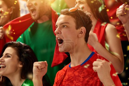Téléchargez les photos : Gens excités et émotionnels, les fans de football portugais encouragent émotionnellement l'équipe préférée pendant le match au stade. Concept de sport, compétition, championnat, émotions, passe-temps et divertissement - en image libre de droit