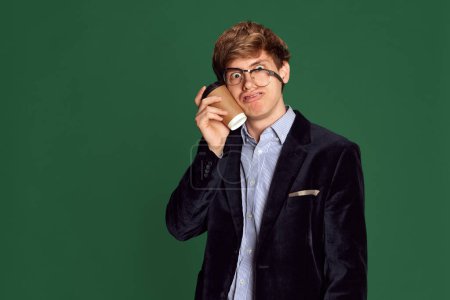 Foto de Plazos. Imagen divertida de hombre joven, trabajador con café y gafas que caen sobre fondo de estudio verde. Un exceso de trabajo. Concepto de negocio, educación, moda, emociones, juventud, estilo de vida - Imagen libre de derechos