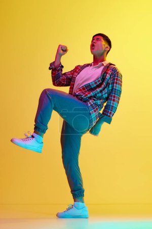 Photo for Young korean guy in stylish casual clothes showing emotions of success, win against yellow background in neon light. Achievement. Concept of human emotions, youth, fashion, lifestyle - Royalty Free Image