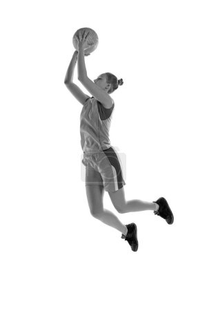 Téléchargez les photos : Image en noir et blanc de la jeune fille sportive en saut, jouant au basket-ball sur fond de studio blanc. Concept de sport professionnel, passe-temps, mode de vie sain, action et mouvement - en image libre de droit