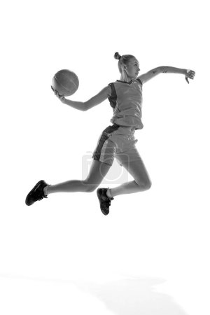 Téléchargez les photos : Image en noir et blanc de la jeune fille sportive pendant le jeu de basket-ball, jouer, s'entraîner sur fond de studio blanc. Concept de sport professionnel, passe-temps, mode de vie sain, action et mouvement - en image libre de droit