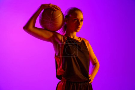 Téléchargez les photos : Portrait de jeune fille athlétique, joueuse de basket en uniforme, posant avec balle sur fond de studio blanc. Concept de sport professionnel, passe-temps, mode de vie sain, action et mouvement - en image libre de droit