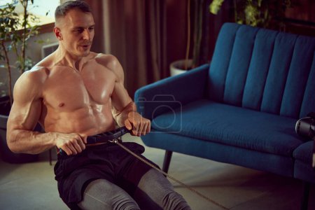 Photo for Handsome young man with relief, muscular body training shirtless, doing exercises with stationary rowing machine. Concept of sportive lifestyle, body and health care, fitness, health - Royalty Free Image