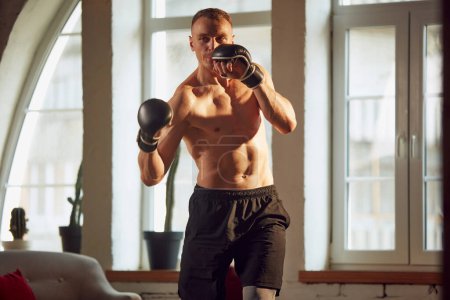 Photo for Sportive man with muscular, relief, strong, attractive body, training shirtless, ding boxing exercises at home on daytime. Concept of sportive lifestyle, body and health care, fitness, health - Royalty Free Image
