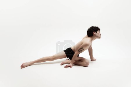 Téléchargez les photos : Image studio de jeune homme posant torse nu en sous-vêtements sur fond blanc. Mâle mince, corps en forme avec tatouage. Concept d'esthétique du corps masculin, style, mode, santé, beauté masculine - en image libre de droit