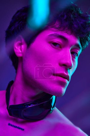 Téléchargez les photos : Portrait de jeune, asiatique, bel homme posant torse nu sur fond de studio violet sous la lumière du néon. Regarde bien. Concept d'esthétique du corps masculin, style, mode, santé, beauté masculine - en image libre de droit