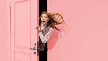 Photo for Young pretty girl peeking out open pink door and looking with positive excitement, astonishment. Surprised look. Good news, sales. Concept of emotions, facial expression, lifestyle - Royalty Free Image