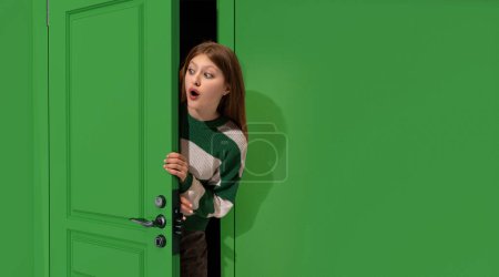 Foto de Chica joven asombrada, adolescente asomándose por la puerta verde con la cara conmocionada, mirando con los ojos abiertos. Sorpresa. Concepto de emociones, expresión facial, estilo de vida, juventud - Imagen libre de derechos