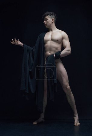 Photo for Full-length portrait of muscular, shirtless, handsome man posing in dark fabric against black studio background. Statue art. Concept of male body aesthetics, mens beauty, inspiration, art - Royalty Free Image