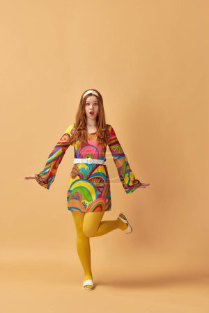 Téléchargez les photos : Portrait complet de belle jeune femme dans des vêtements colorés élégants posant sur fond de studio orange. Concept de style rétro, mode, beauté, élégance, années 60, jeunesse. Style pin-up - en image libre de droit