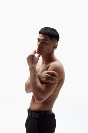 Téléchargez les photos : Portrait de jeune homme asiatique beau posant torse nu dans un pantalon sur fond de studio blanc. Visage immaculé, corps musclé. Concept de beauté masculine, soins de la peau, cosmétologie, santé masculine - en image libre de droit