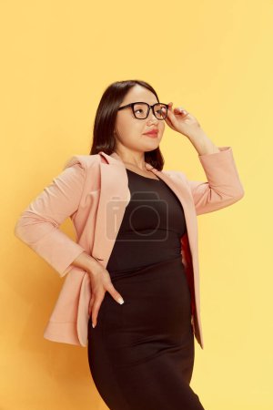 Téléchargez les photos : Portrait de femme confiante, jeune, asiatique en tenue formelle et lunettes sur fond de studio jaune. J'attends avec impatience le succès. Concept d'émotions, mode de vie, jeunesse, affaires et éducation - en image libre de droit