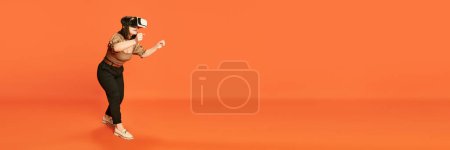 Téléchargez les photos : Portrait de jeune fille portant des verres VR et playin g vide jeux en ligne sur fond de studio orange. Je conduis. Concept d'émotions, mode de vie, jeunesse, technologies modernes. Bannière. Espace de copie pour la publicité - en image libre de droit