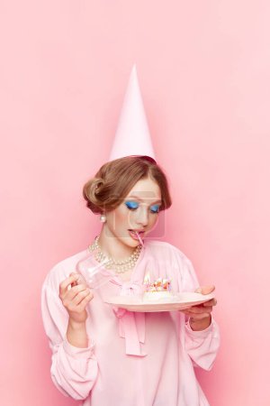 Foto de Elegante, hermosa, joven con maquillaje abriendo su pastel de cumpleaños sobre fondo de estudio rosa. Pide tu deseo. Fotografía de arte pop de comida. Concepto de estilo retro, visión creativa, imaginación. - Imagen libre de derechos