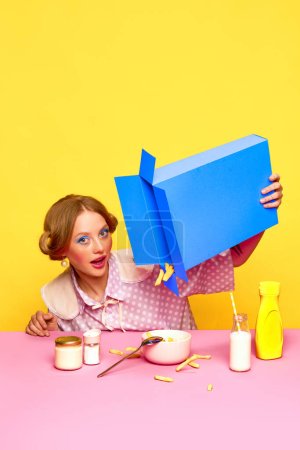 Fast food lover. Pretty young girl with bright makeup pouring fries from box against yellow studio background. Food pop art photography. Concept of retro style, creative vision. Complementary colors