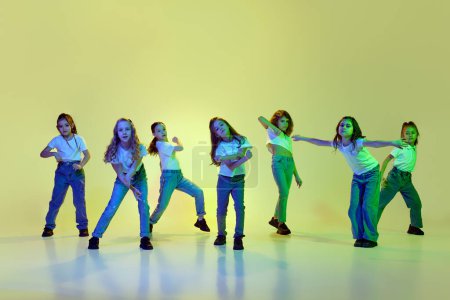 Photo for Talented, active, little girls, children dancing hip-hop in sportive casual clothes against green studio background in neon light. Concept of childhood, hobby, sportive lifestyle, active and motion - Royalty Free Image